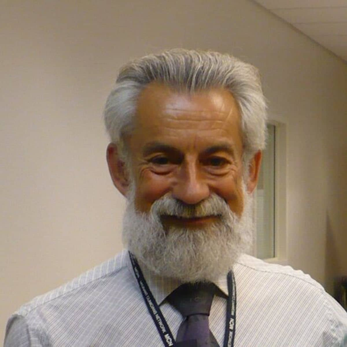 2024 TB Champion Dr. Ed Zuroweste smiling, wearing a button up and blue tie, with grey hair and beard