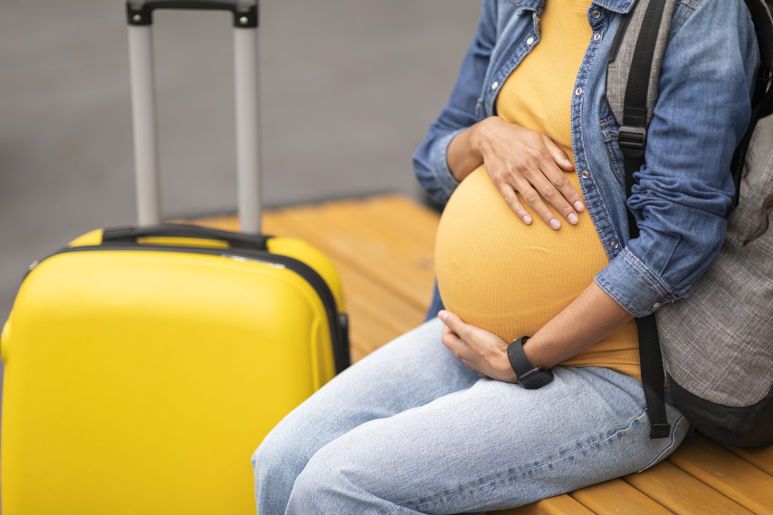 Pregnant traveler holding pregnant belly with both hands.