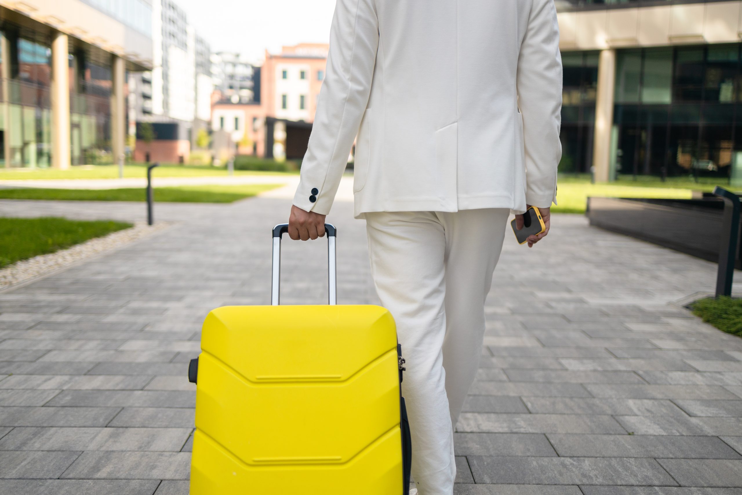 Traveler in suit pulling a yellow suitcase.