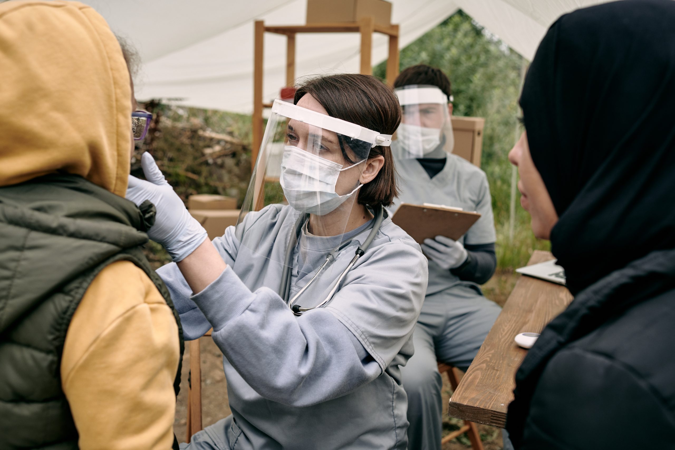 Healthcare professionals with protective gear medically examining patients in a field setting.