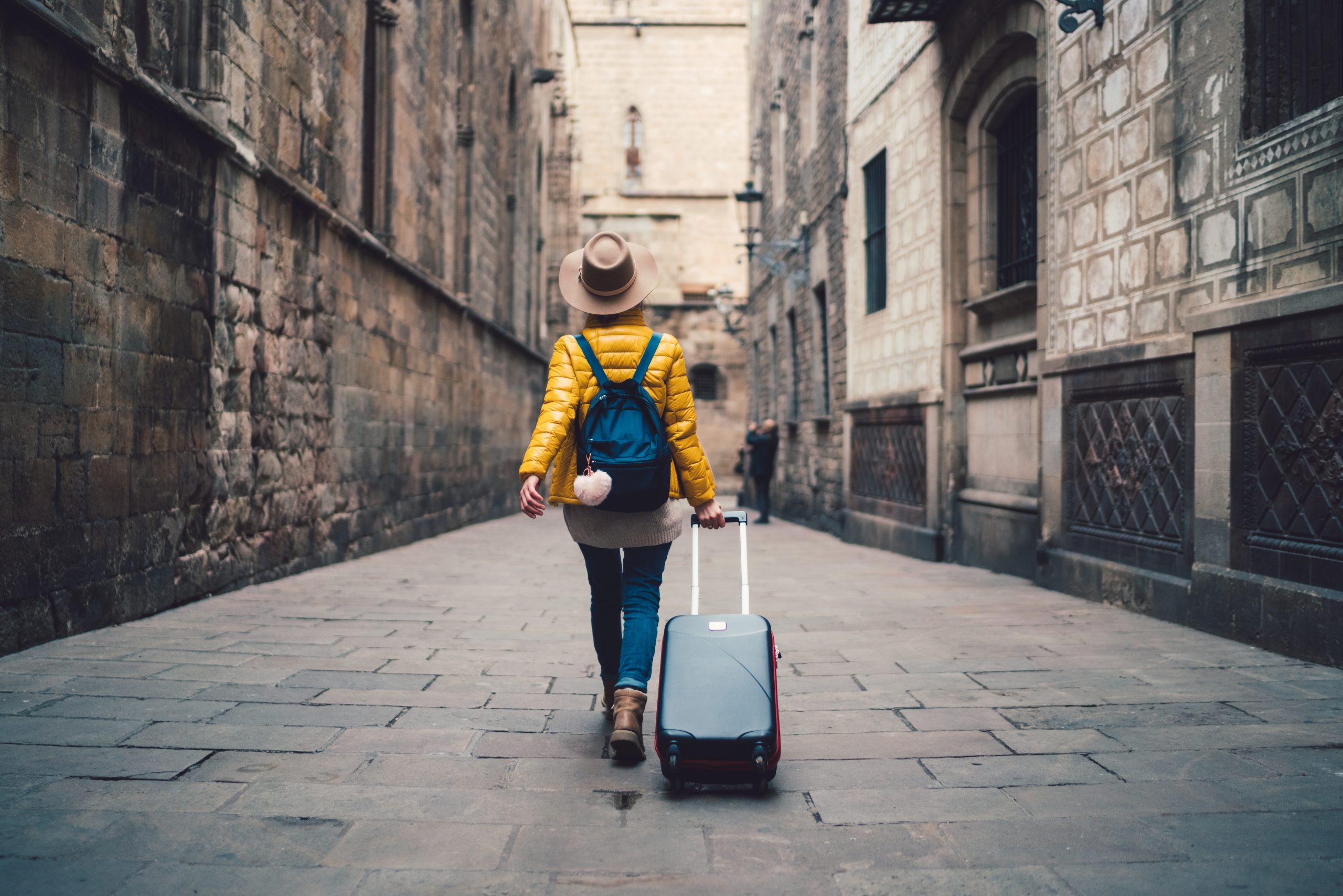 Young traveler pulling a suitcase down an alley.