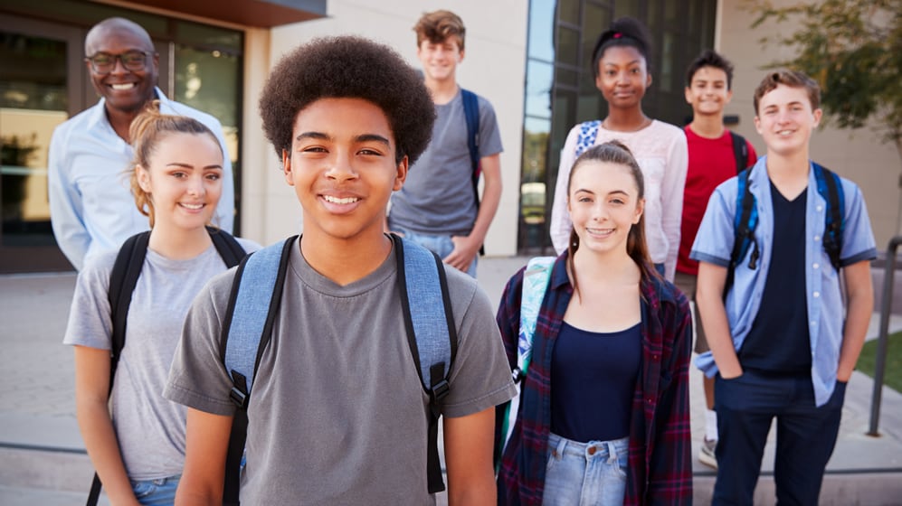 A group of high school students standing in front of school building with a teacher.