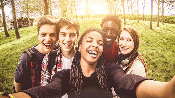 Five teenagers in a park smiling as they take a picture of themselves.