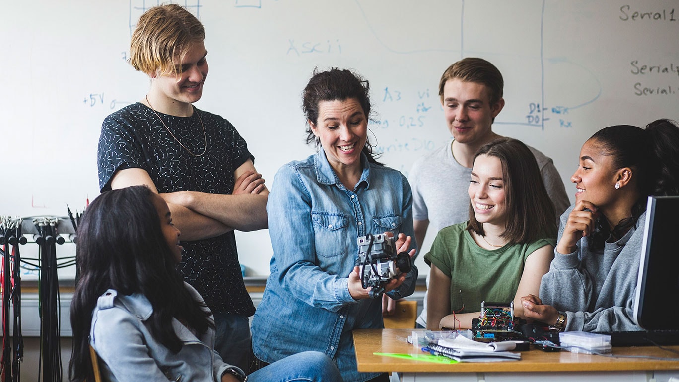 A female teacher explaining how to use a camera to high school students in classroom.