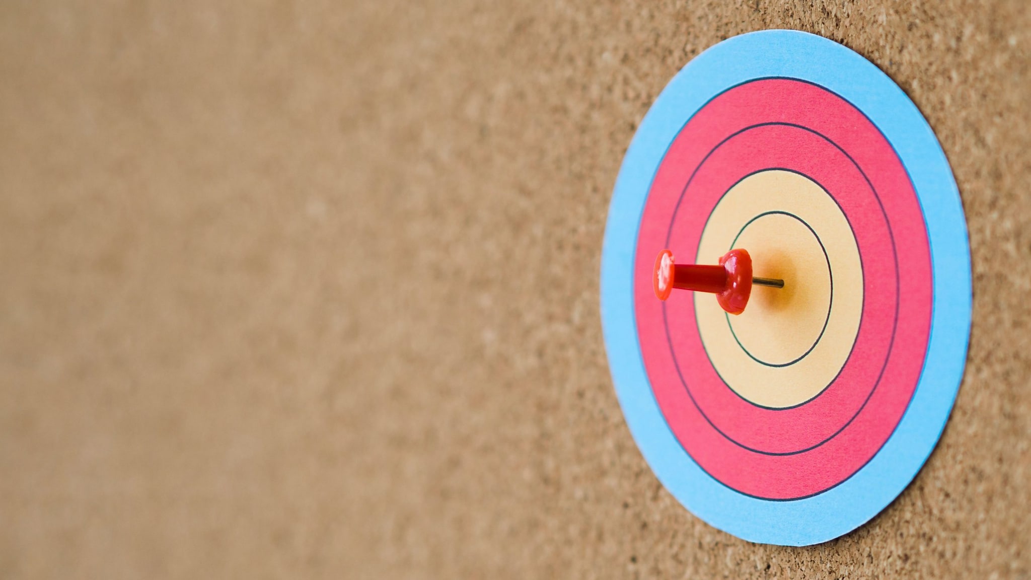 A corkboard with a paper target attached and a push pin in the center.