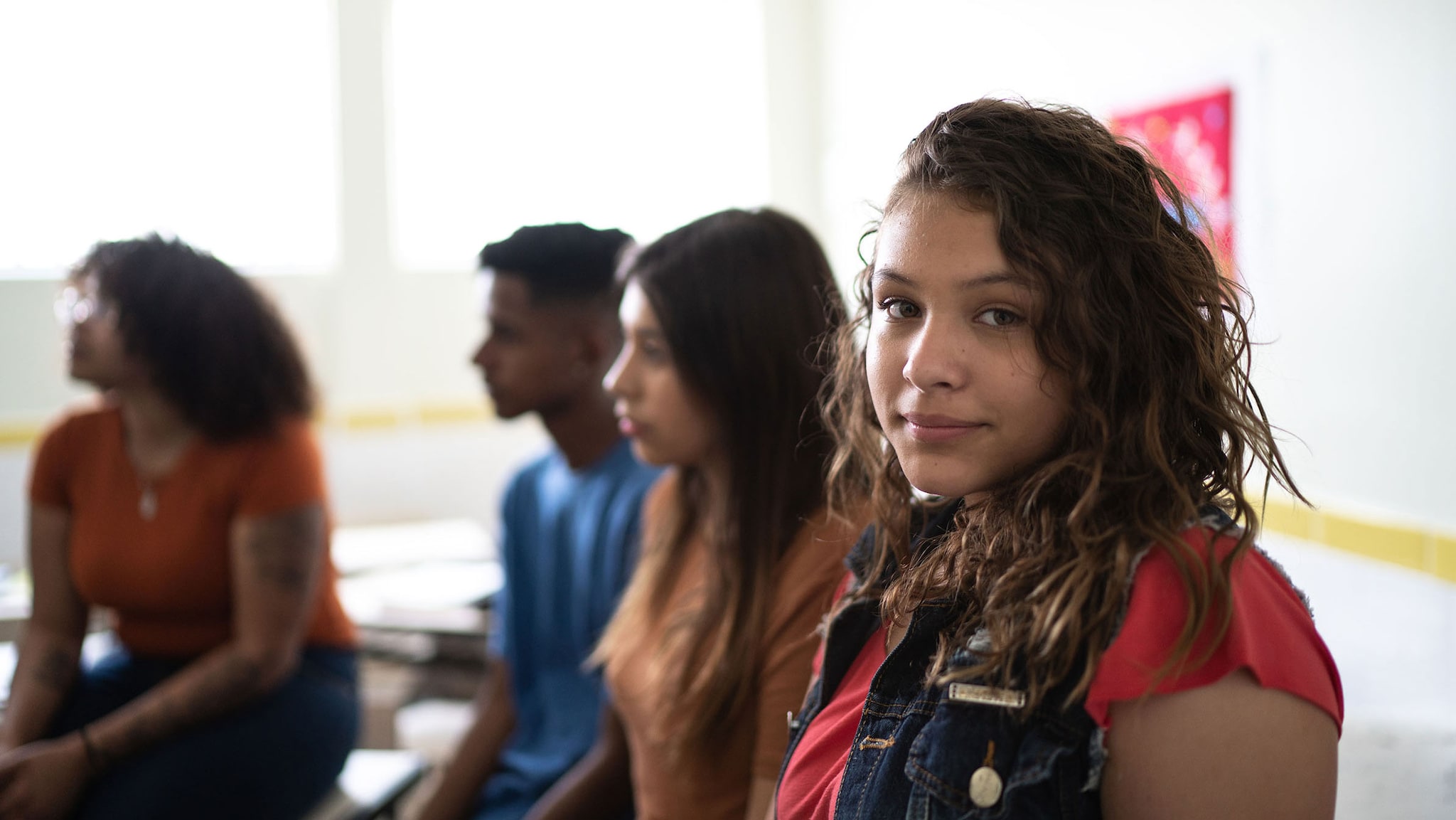 Portrait of a female teenage student in classroom, with a group of diverse students beside her.